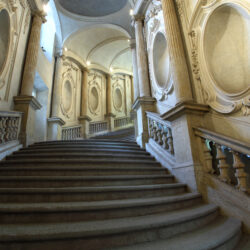 Lo scalone guariniano di Palazzo Carignano, in morbide linee curve che definiscono l’andamento delle rampe, dei gradini e delle nicchie che favoriscono suggestivi chiaroscuri, permetteva di accedere alla sala da ballo, rimaneggiata nell’Ottocento per ospitare il Parlamento Subalpino. Gli stucchi si devono a Pietro Somasso.