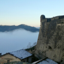 Il Forte e le colline del parco del Neirone sembrano galleggiare in un mare di nuvole, dialogando sui promontori del Gaviese; dal bastione San Tommaso si ammirano il bastione della mezzaluna che ospita la polveriera, di cui si vede il tetto, e il fianco del bastione San Giovanni Battista con la garitta d’angolo.
Nella veduta di scorcio si leggono alcune delle varie fasi storiche che hanno caratterizzato il Forte, con sovrapposizioni realizzate tra il XVII e il XVIII secolo.